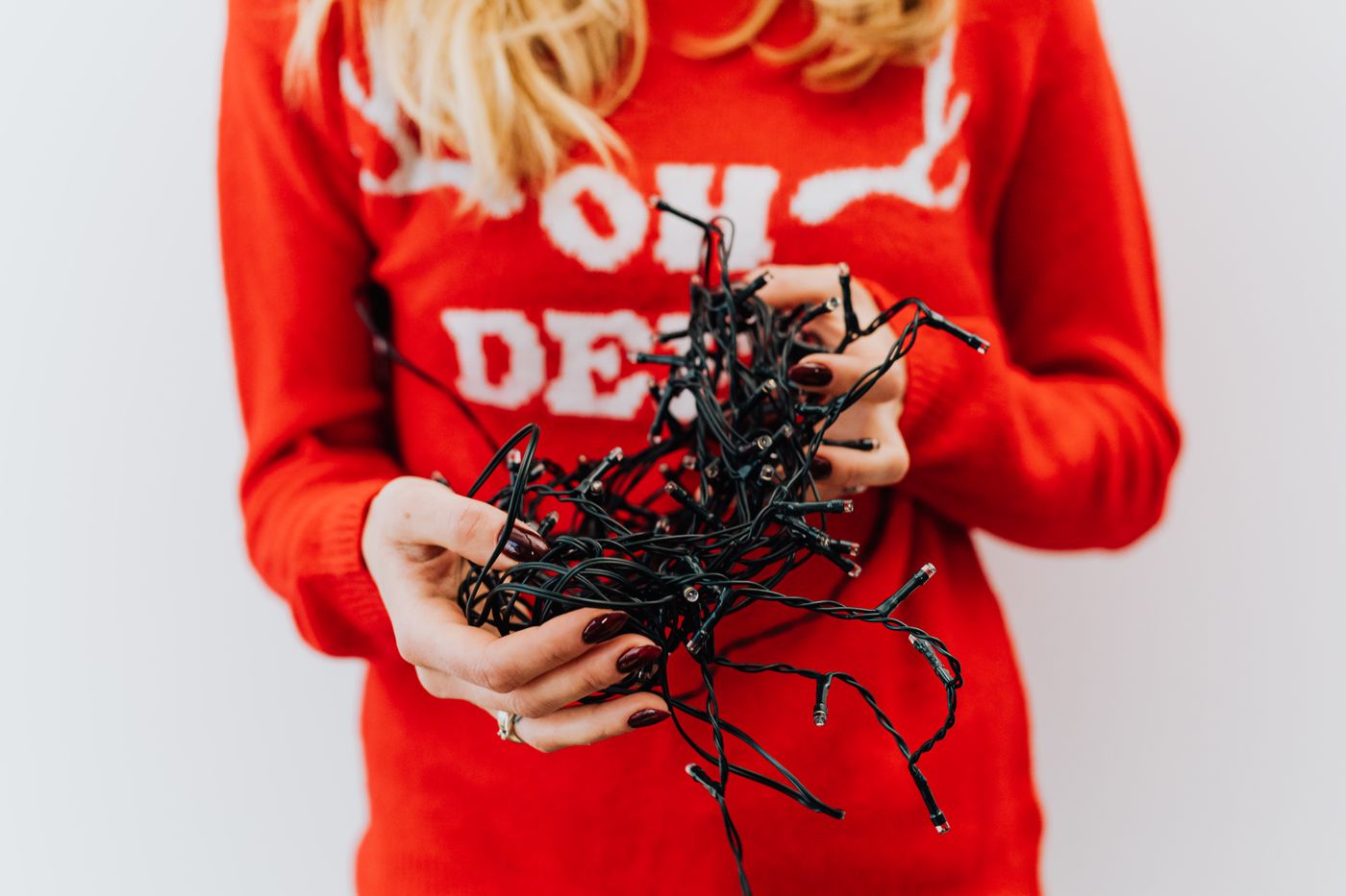 A homeowner in a festive red sweater holding a big tangle of Christmas lights